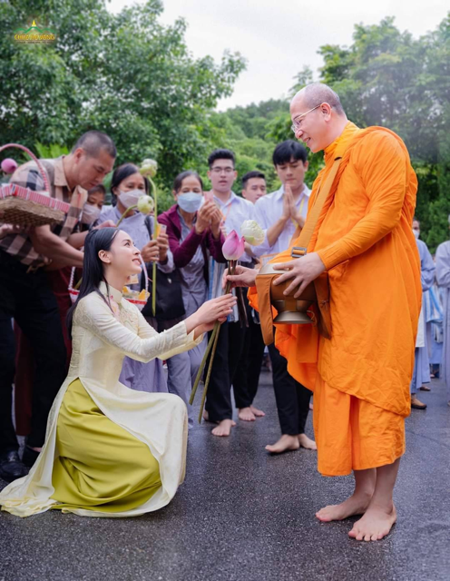 A person in an orange robe kneeling down to a person in an orange robe
Description automatically generated